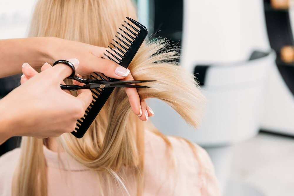 cropped image of hairdresser trimming ends of blonde hair