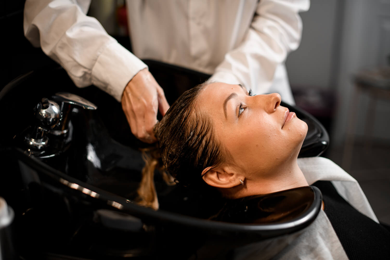 Close-up of caucasian female client relaxed lying on hair washing chair while hairdresser washes her hair